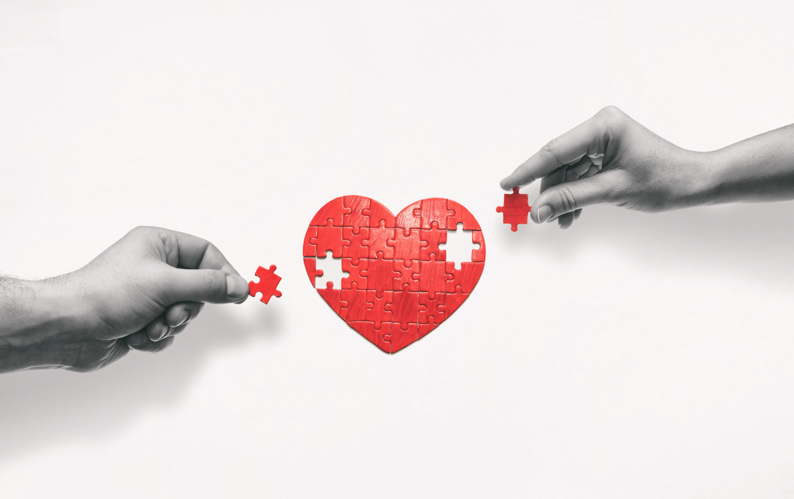 Two hands shown putting together a heart shaped jigsaw puzzle